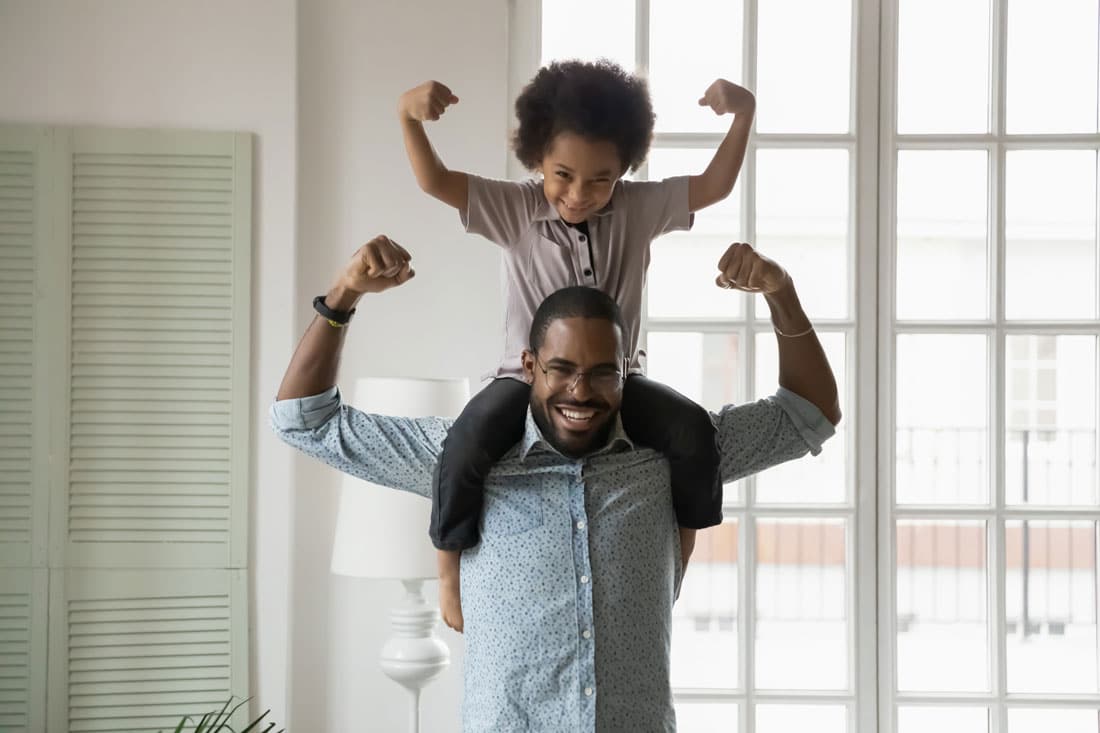 Black father holding son on shoulder making strong arms